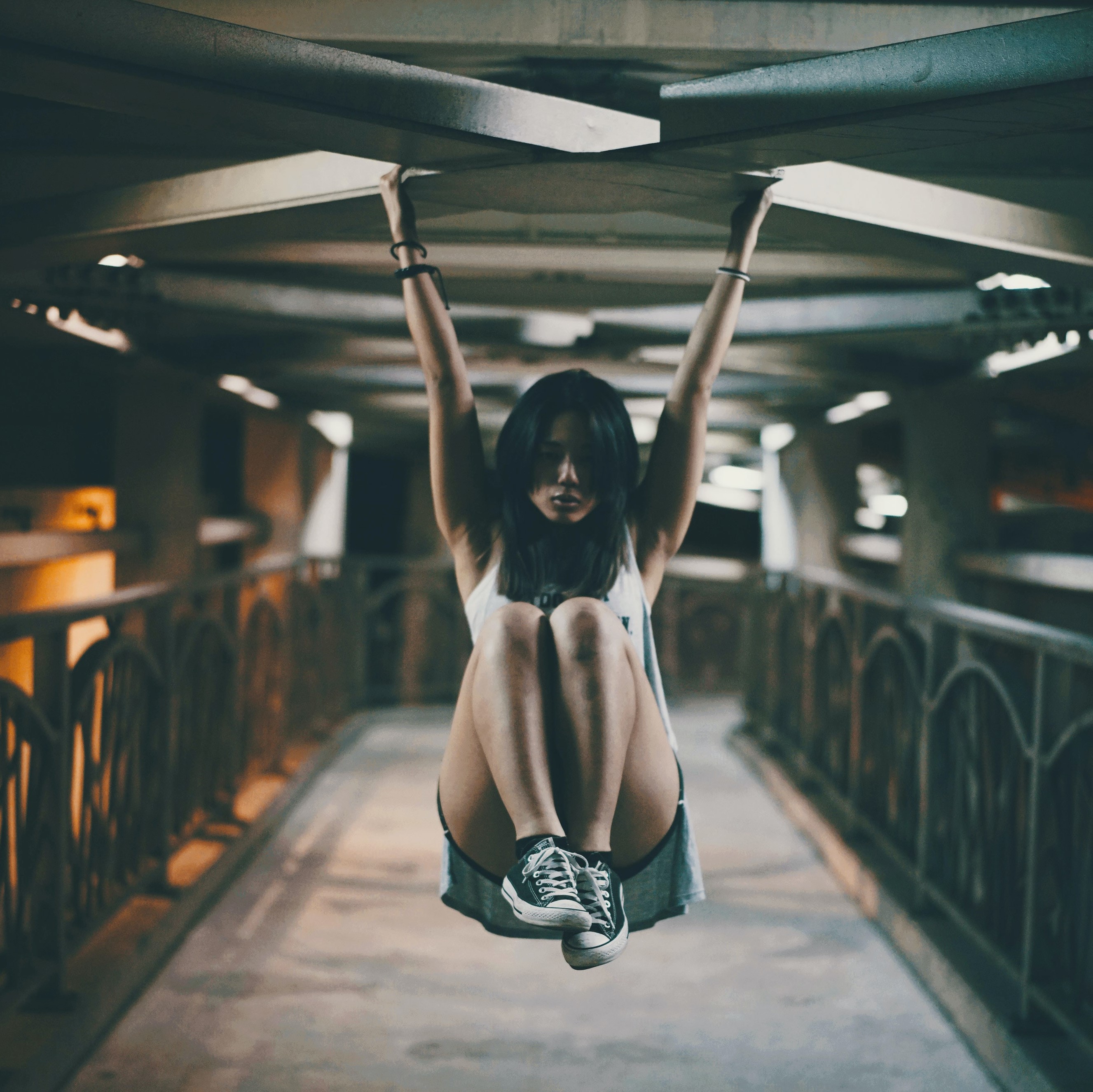 a photo of an athlete hanging by her arms from the rafters of a bridge