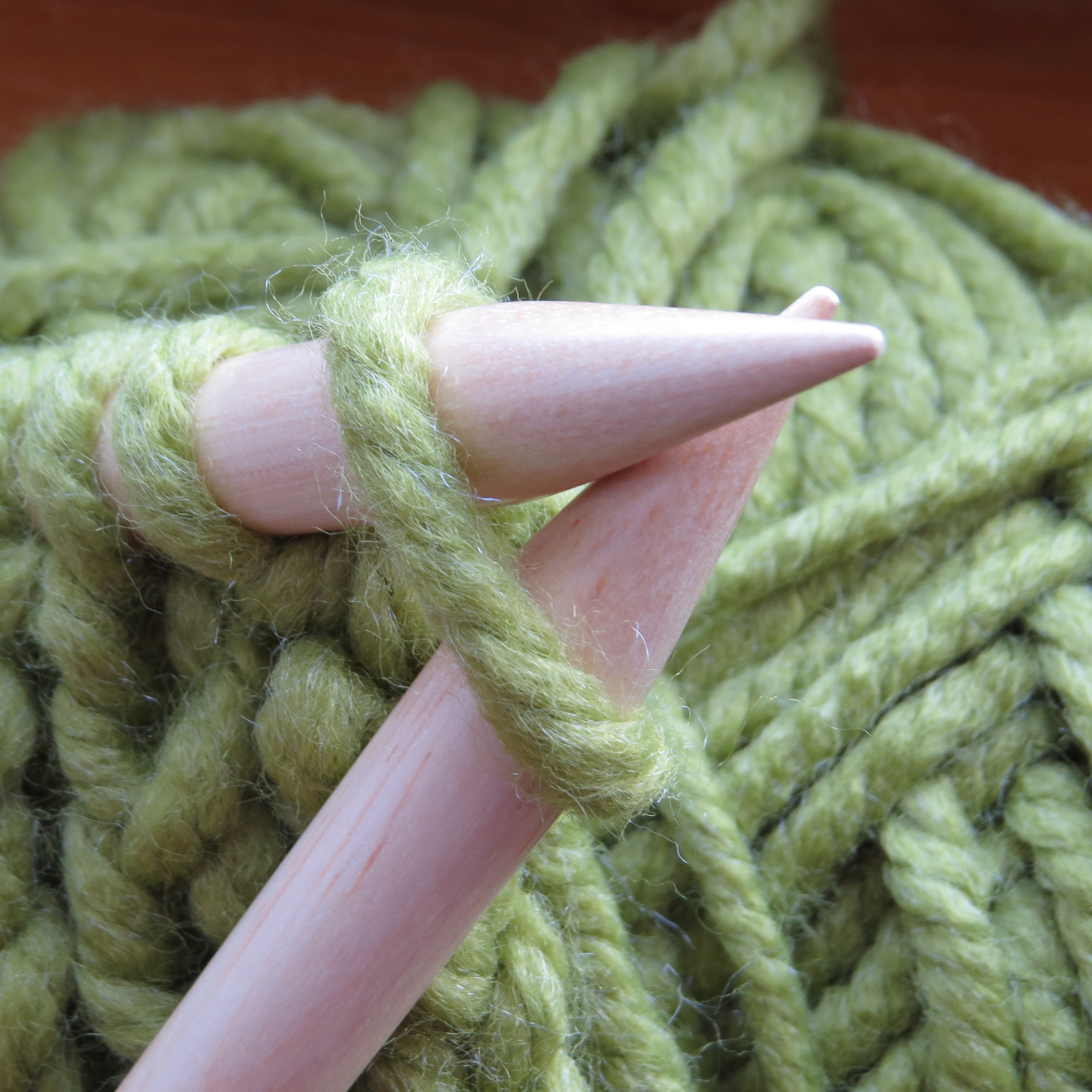 a close up photo of yarn being knitted with thick needles